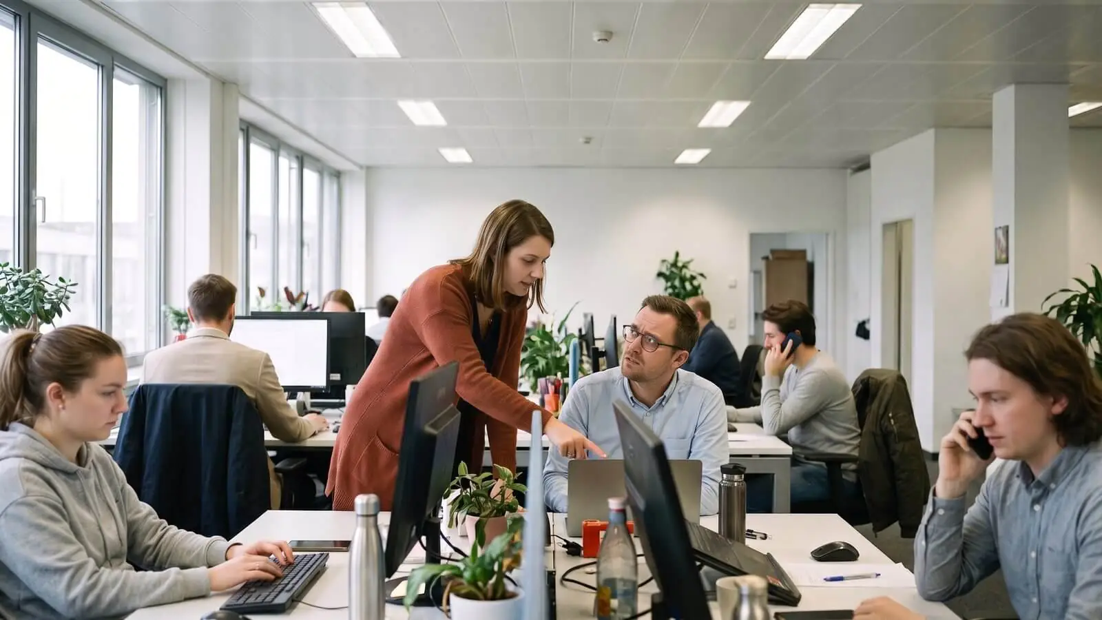 Two colleagues discussing figures at a desk in a busy open-plan office